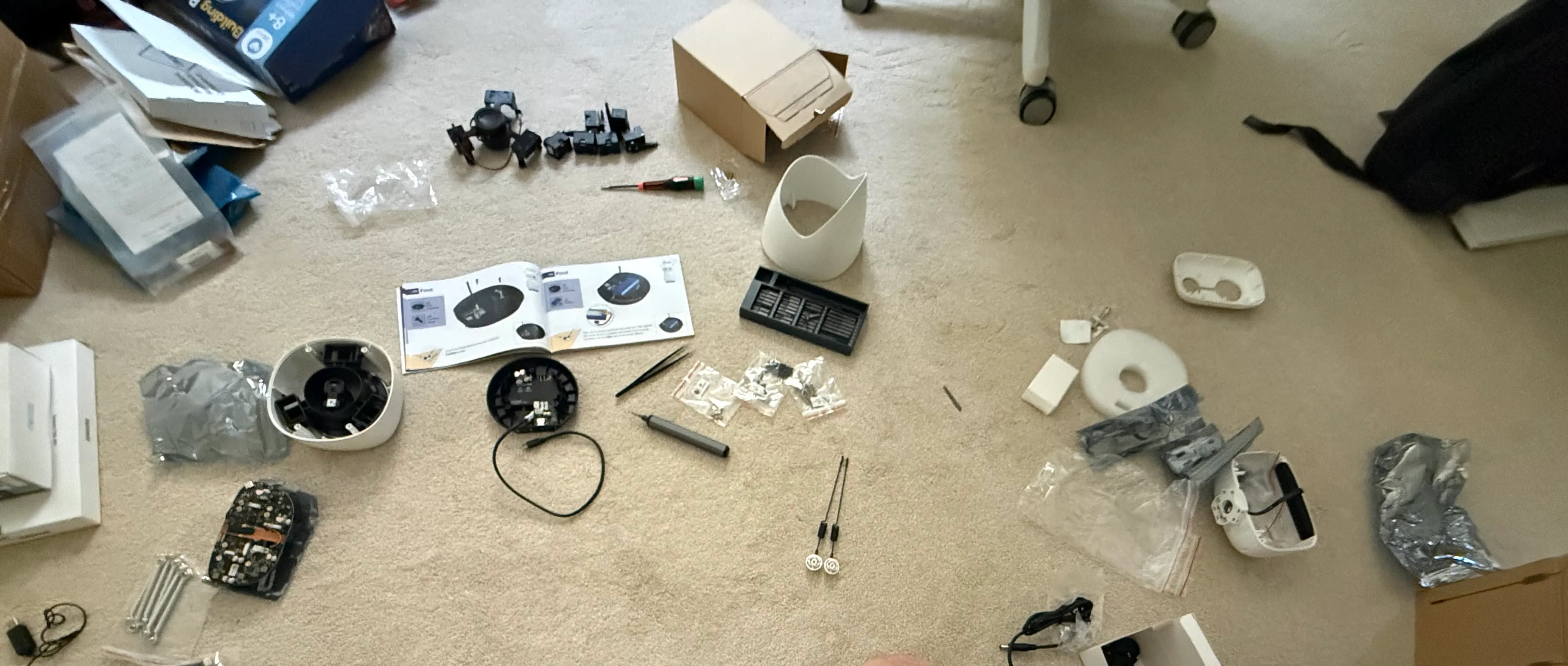 The Reachy Mini kit mid-build: parts, manual, shell halves and toolkit laid out in a circle on the carpet
